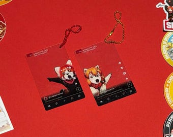 May include: Two rectangular clear acrylic keychains with red backgrounds featuring anime-style characters. Each keychain has a metal ball chain, social media interface graphics, and the text SFU INTERACTIVE ARTS AND TECHNOLOGY printed at the top.