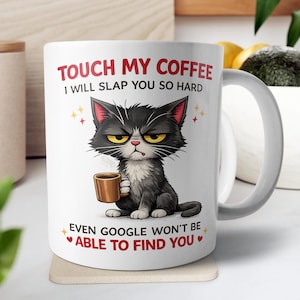 May include: A white ceramic mug with a black handle and the text "But First, Coffee" in a black, bold font. The mug is sitting on a wooden surface. The mug is approximately 4 inches tall.