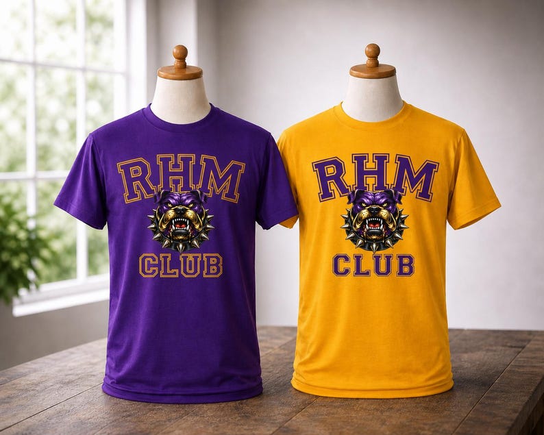 Op de afbeelding: Twee t-shirts op mannequins. E&eacute;n is paars, de andere is goudkleurig. Beide hebben de tekst "RHM CLUB" in gouden letters met een bulldog-afbeelding. De bulldog is paars en goud met een spijkerhalsband. De shirts worden op een houten tafel getoond.
