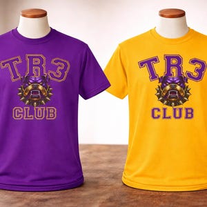 Op de afbeelding: Twee T-shirts met korte mouwen op paspoppen. De ene is paars, de andere is geel. Beide shirts hebben de tekst "TR3 CLUB" in een lettertype in collegestijl, met een bulldog-afbeelding in het midden.