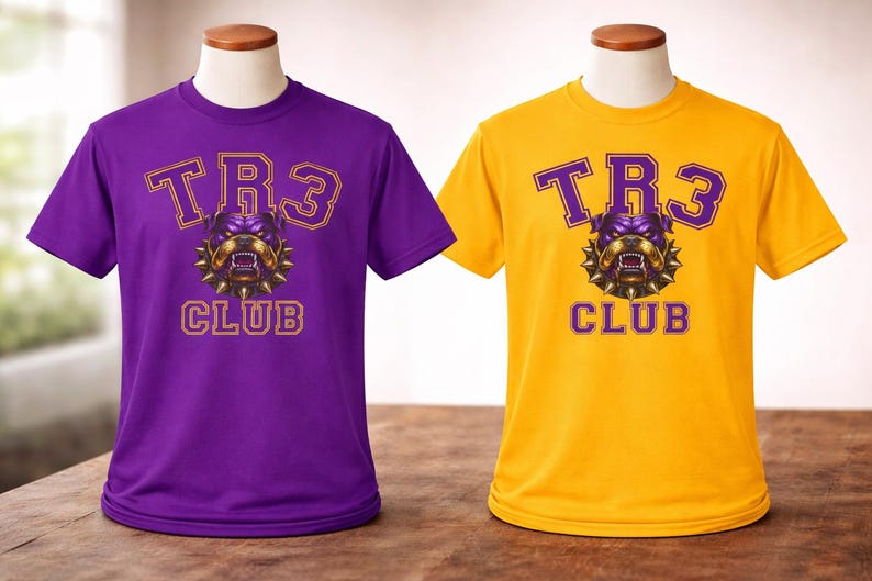 Op de afbeelding: Twee T-shirts met korte mouwen op paspoppen. De ene is paars, de andere is geel. Beide shirts hebben de tekst "TR3 CLUB" in een lettertype in collegestijl, met een bulldog-afbeelding in het midden.
