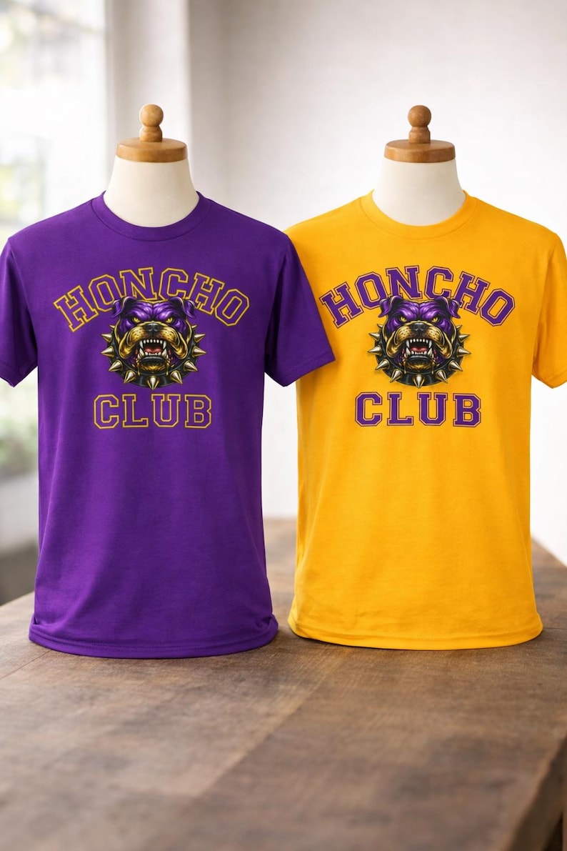 Op de afbeelding: Twee t-shirts, &eacute;&eacute;n paars en &eacute;&eacute;n goud, gepresenteerd op mannequins. Elk shirt heeft de tekst "HONCHO CLUB" boven een bulldog-afbeelding. De bulldog is paars en goud met een spiked kraag. De tekst is goud.
