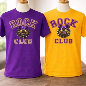 Op de afbeelding: Twee T-shirts, &eacute;&eacute;n paars en &eacute;&eacute;n geel, elk met de tekst "ROCK CLUB" boven en onder een bulldog-afbeelding. De bulldog is paars en goud, met een spijkerhalsband. De shirts worden op mannequins getoond.