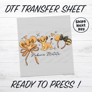 May include: DTF transfer sheet featuring Simba from The Lion King. The design includes Simba, a bow, and mouse ears with the text "Hakuna Matata". The sheet also includes the text "Ready to Press!" and "Ships Next Day".