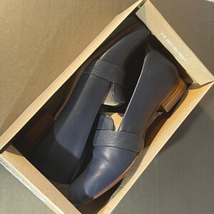 May include: A pair of navy blue leather loafers with a textured strap detail, presented inside a cardboard box. The shoes have a low wooden heel and a classic design, suitable for various occasions. The box has text that reads "#19 280x160x100mm".