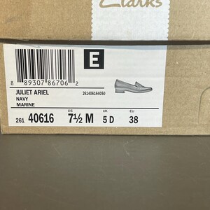 May include: A brown cardboard shoe box with a label displaying product information. The label includes the text "JULIET ARIEL NAVY MARINE", a barcode, and shoe size details: US 7 1/2 M, UK 5 D, and EU 38. A small illustration of a shoe is also present.
