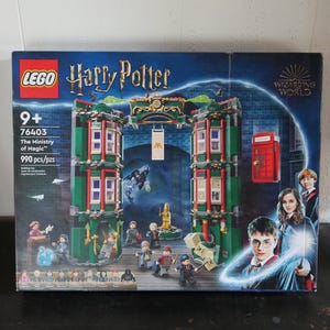May include: A LEGO Harry Potter building set box featuring the Ministry of Magic. The box is predominantly blue, green, and red, with images of characters and the building set. Text includes "LEGO", "Harry Potter", "The Ministry of Magic", and "990 pcs/pzs".
