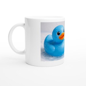 Op de afbeelding: Witte keramische mok met een afbeelding van een blauwe badeend met een oranje snavel. De eend wordt afgebeeld in een bruisende, waterige omgeving. Een leuk en grillig item voor elke drank.