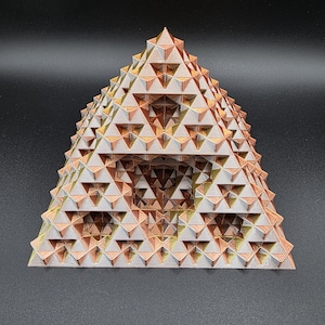 May include: A 3D-printed fractal pyramid in shades of copper, gold, and silver. The geometric structure features repeating triangular patterns, creating a complex and visually appealing design. The pyramid is a decorative object.