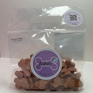 May include: A clear plastic bag filled with dog treats. The treats are bone and heart-shaped, with a light brown color. The bag has a label that reads "Chicken & Beet 3.53 oz 100 gr" and a circular sticker with the text "Furtasty Bakery".