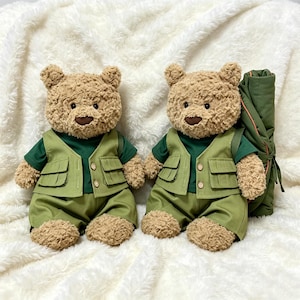 May include: Two plush teddy bears with light brown curly fur, dark brown noses, and black eyes. Each bear wears a dark green short-sleeved shirt, a light olive green utility vest with two front pockets and two buttons, and matching olive green shorts.