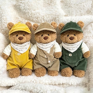 Op de afbeelding: Drie pluche teddyberen in bijpassende outfits bestaande uit een corduroy pet, een wit shirt met korte mouwen, een witte bandana met kleine bruine berenprints en een corduroy tuinbroek in de kleuren geel, beige en donkergroen.