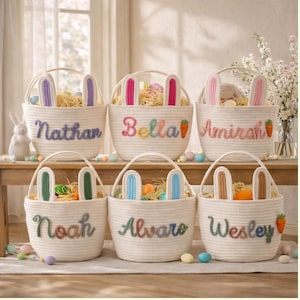 May include: Six white rope Easter baskets with bunny ears, each personalized with a name in colorful embroidery. The baskets are filled with straw and Easter eggs. A carrot is embroidered on some baskets.