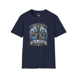 Può includere: T-shirt blu navy con una grafica di un cane poliziotto pastore tedesco e la scritta "Louisville Police K-9 Unit". Il design include un paesaggio urbano e le parole "River City's Finest, Steadfast and Loyal".