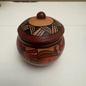 May include: A small, round, hand-painted ceramic jar with a lid. The jar is primarily red with orange and black geometric designs. The lid has a dark brown knob and a decorative pattern.