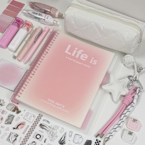 Könnte beinhalten: Ein spiralgebundenes Notizbuch mit einem rosafarbenen Verlaufscover und dem Text Life is a leaf of paper white sowie ONE DAY'S everything will pass. Dazu gehören ein weißes, gestepptes Federmäppchen, rosa und weiße Stifte, Klebeband, Aufkleber und ein Sternanhänger.
