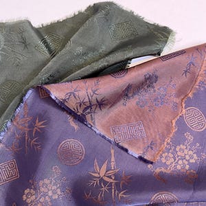 May include: Close-up of three pieces of fabric with an oriental design. The fabric is in shades of purple, olive green, and peach. The design includes bamboo, flowers, and geometric shapes. The fabric has a slight sheen and a frayed edge.