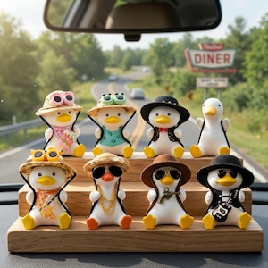 Könnte beinhalten: Eine Sammlung von acht dekorativen Entenfiguren, jede mit einzigartigen Accessoires. Die Enten sind weiß mit gelben Schnäbeln und Füßen und tragen Hüte, Sonnenbrillen und Outfits. Sie sind auf einer Holzablage angeordnet, mit einer Straße und einem Diner-Schild im Hintergrund.