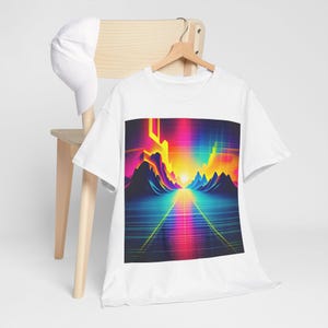 Puede incluir: Camiseta blanca con un diseño de paisaje retro. El gráfico muestra una escena futurista colorida con montañas, una cuadrícula y un sol brillante, que evoca los años 80. Una gorra de béisbol blanca descansa sobre una silla de madera.