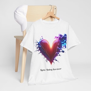 Puede incluir: Camiseta blanca con un diseño de corazón vibrante en tonos rojos, morados y azules. El corazón está rodeado de formas abstractas y el texto "Sync Swing Survivor" está impreso debajo. Una gorra de béisbol blanca descansa sobre una silla de madera.