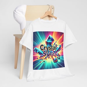 Puede incluir: Camiseta blanca con un diseño gráfico colorido. El diseño presenta un grupo de cristales azules y turquesas con el texto "Crystal Synic". El fondo tiene una luz radiante naranja, amarilla y azul.
