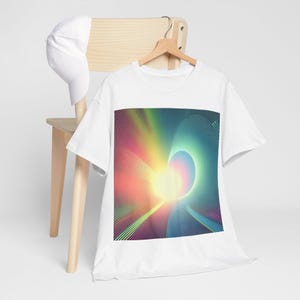 Puede incluir: Camiseta blanca con un diseño abstracto colorido. El gráfico presenta un espectro de colores, incluyendo amarillo, rosa, azul y verde, con un patrón radial de líneas curvas. Una gorra de béisbol blanca descansa sobre una silla de madera.