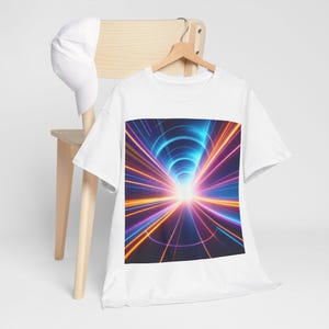 Puede incluir: Camiseta blanca con un gráfico colorido de un túnel de luz. El diseño muestra una fuente de luz central brillante con líneas radiantes en tonos de azul, naranja y morado. Una gorra de béisbol blanca descansa sobre una silla de madera.