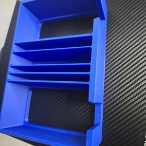 Puede incluir: Un organizador azul brillante, impreso en 3D, con m&uacute;ltiples estantes horizontales. El marco rectangular tiene lados abiertos y est&aacute; dise&ntilde;ado para guardar objetos peque&ntilde;os. El pl&aacute;stico tiene una superficie ligeramente texturizada.