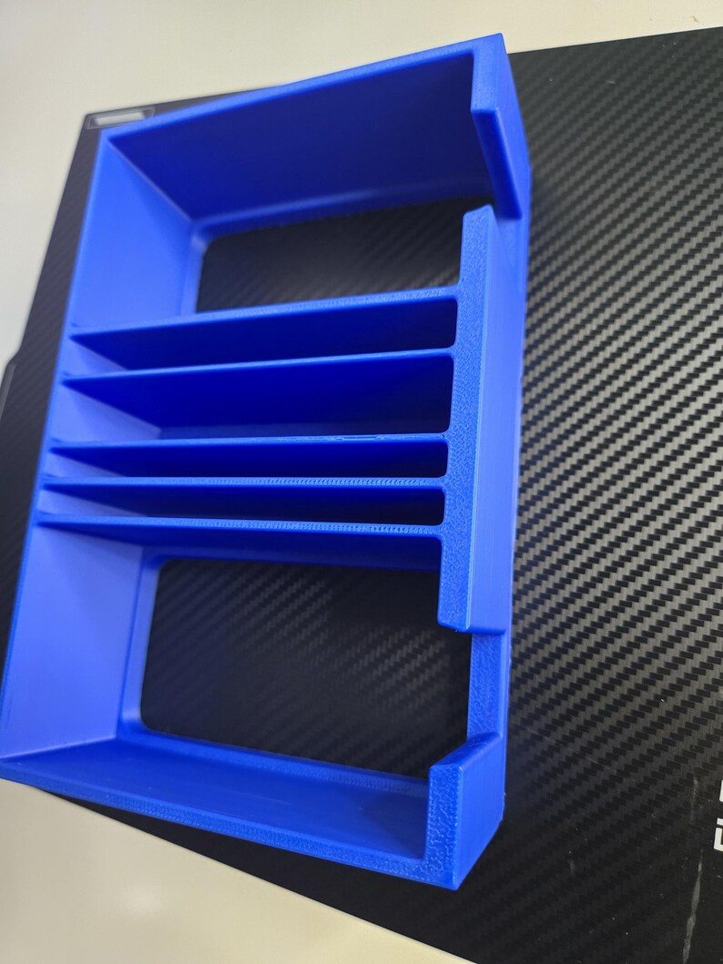 Puede incluir: Un organizador azul brillante, impreso en 3D, con m&uacute;ltiples estantes horizontales. El marco rectangular tiene lados abiertos y est&aacute; dise&ntilde;ado para guardar objetos peque&ntilde;os. El pl&aacute;stico tiene una superficie ligeramente texturizada.