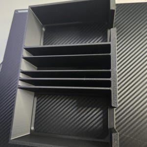 Puede incluir: Un organizador negro con m&uacute;ltiples compartimentos de forma rectangular. El organizador tiene varios estantes horizontales y una estructura en forma de caja. El art&iacute;culo est&aacute; hecho de un material negro mate y est&aacute; dise&ntilde;ado para el almacenamiento y la organizaci&oacute;n.