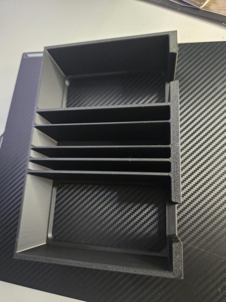 Puede incluir: Un organizador negro con m&uacute;ltiples compartimentos de forma rectangular. El organizador tiene varios estantes horizontales y una estructura en forma de caja. El art&iacute;culo est&aacute; hecho de un material negro mate y est&aacute; dise&ntilde;ado para el almacenamiento y la organizaci&oacute;n.