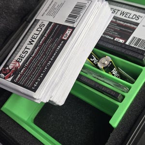 Puede incluir: Una pila de lentes de protecci&oacute;n para soldadura blancos, etiquetados como "BEST WELDS" y "SP-1". Las lentes est&aacute;n en una bandeja verde dentro de un estuche negro, junto con una bater&iacute;a y otros objetos peque&ntilde;os. El embalaje incluye texto en ingl&eacute;s, franc&eacute;s y espa&ntilde;ol.