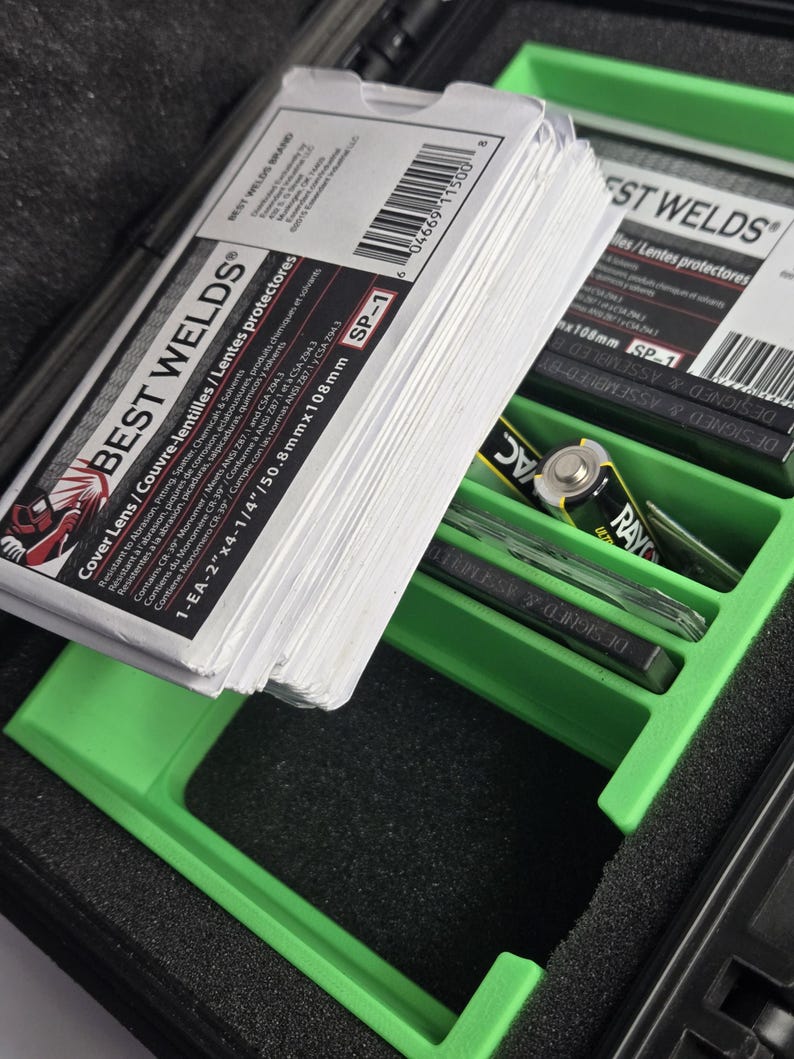 Puede incluir: Una pila de lentes de protecci&oacute;n para soldadura blancos, etiquetados como "BEST WELDS" y "SP-1". Las lentes est&aacute;n en una bandeja verde dentro de un estuche negro, junto con una bater&iacute;a y otros objetos peque&ntilde;os. El embalaje incluye texto en ingl&eacute;s, franc&eacute;s y espa&ntilde;ol.