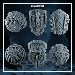 Könnte beinhalten: Ein Set aus sechs grauen Schulterpanzern aus Kunstharz für Miniaturfiguren mit verschiedenen Designs, darunter ein Wolfskopf, ein Schädel, Fellstrukturen und geometrische Muster. Der Text WARGAMESPRINT ist oben im Bild zu sehen.