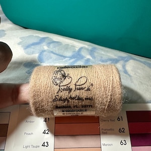 Puede incluir: Un carrete de hilo de bordar marrón claro con la marca "Pretty Punch" visible. La etiqueta también incluye el texto "Washable" y "Dryable". Un gráfico de color con varios tonos está en el fondo.