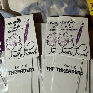 May include: Multiple packages of KA-1100 threaders for punch embroidery. Each package has a white label with the text "Excellence in Punch Embroidery!" and "Pretty Punch." The threaders are thin, silver wires.