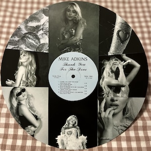 May include: A black and white collage featuring a vintage vinyl record with the text "MIKE ADKINS Thank You For The Dove." The record is surrounded by black and white images of a woman. The collage includes images of lips and a bejeweled arm.