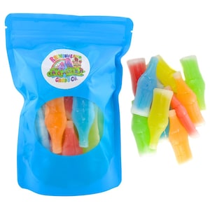 May include: A blue plastic bag filled with colorful, bottle-shaped gummy candies. The bag has a clear window showing the candies inside. A sticker on the bag reads "Rainbowland Candy Co." with a colorful graphic. Several candies are outside the bag.
