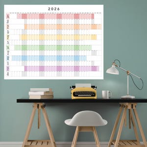 Peut inclure: Un grand calendrier mural pour l'année 2026, avec une mise en page horizontale colorée. Le calendrier affiche les mois et les jours avec un arc-en-ciel de couleurs. Une machine à écrire jaune, des livres et une lampe de bureau sont sur un bureau noir.