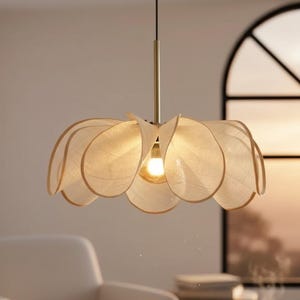Puede incluir: Una lámpara colgante decorativa con diseño de flor. Tiene un tallo dorado y pantallas en forma de pétalo en beige claro con un borde beige más oscuro. La bombilla es visible en el centro de la lámpara.