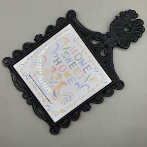 Pode incluir: Uma caneca de cerâmica branca com uma alça preta e o texto "But First, Coffee" em negrito preto. A caneca está sobre um fundo desfocado, sugerindo um ambiente acolhedor.