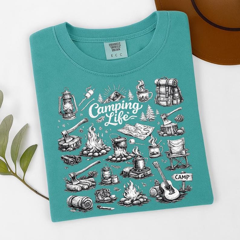 May include: Teal-colored t-shirt with a camping-themed graphic. The design features illustrations of camping gear, including a lantern, axes, a campfire, a guitar, and the words "Camping Life".