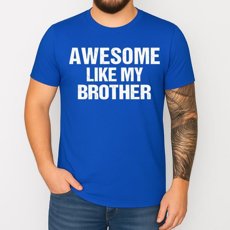 May include: A royal blue t-shirt with the white text "AWESOME LIKE MY BROTHER". The shirt is a crew neck style and appears to be made of a soft material. The text has a slightly distressed appearance.