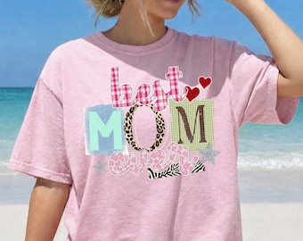 May include: A light pink t-shirt with the words "best MOM ever" in a colorful design. The word "best" is in a pink plaid pattern, the "O" in "MOM" has a leopard print, and the "M" is green and brown.