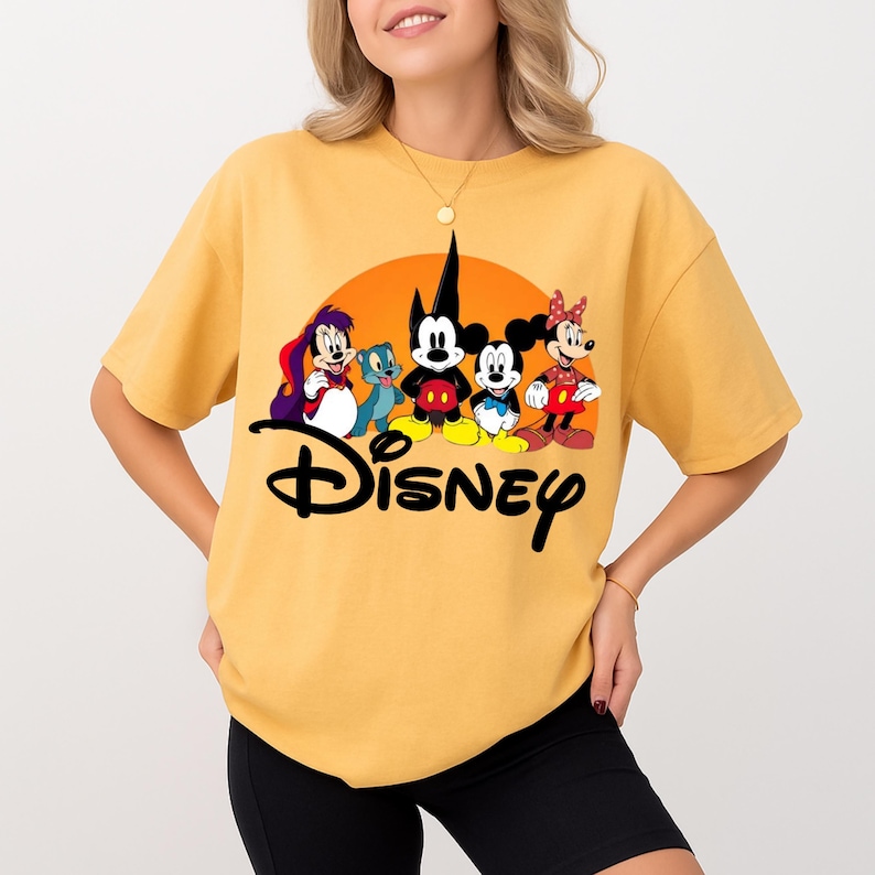 May include: Mustard yellow t-shirt featuring a Disney graphic. The graphic includes Mickey Mouse, Minnie Mouse, and other Disney characters in a colorful design. The word "Disney" is written in a black script font.