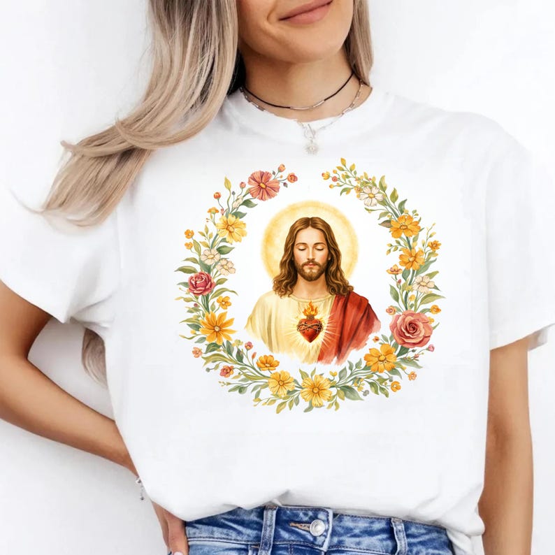 K&ouml;nnte beinhalten: Wei&szlig;es T-Shirt mit einer Aquarellillustration von Jesus, umgeben von einem Blumenkranz. Das Bild enth&auml;lt ein Herz mit Flammen. Das Design ist mittig auf dem T-Shirt platziert.