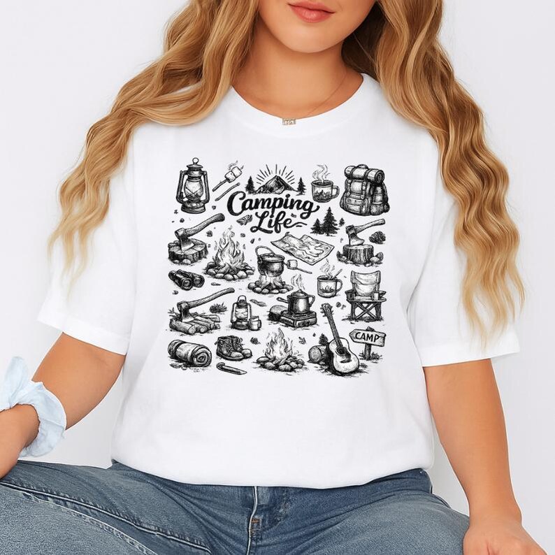 May include: White t-shirt featuring a black and white illustration of camping-related items. The design includes a campfire, tent, lantern, backpack, guitar, and the words "Camping Life".