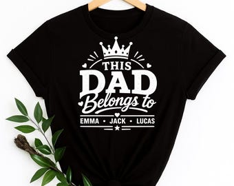 May include: A black short-sleeved t-shirt featuring white graphic text that reads THIS DAD Belongs to EMMA • JACK • LUCAS. The design includes a crown icon at the top, small heart accents, and horizontal lines, all printed on the front of the shirt.