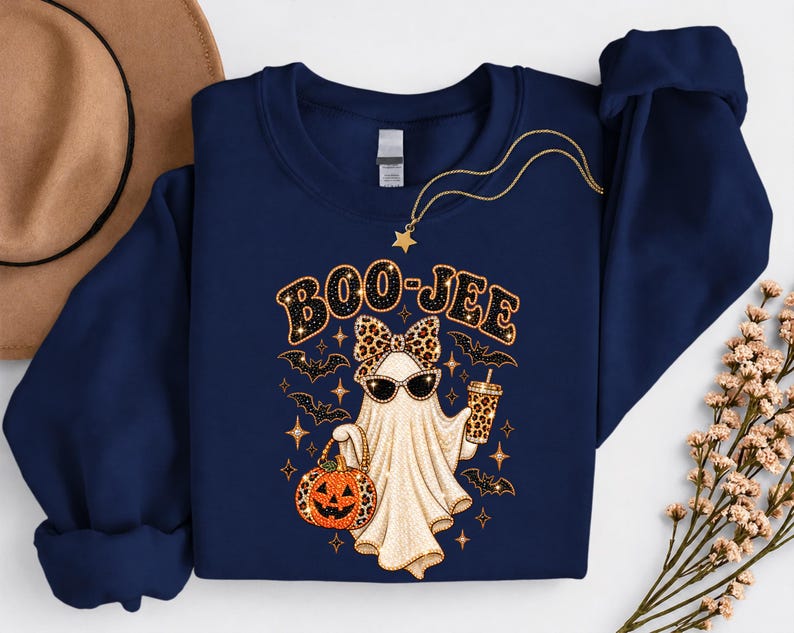 Pu&ograve; includere: Una felpa blu navy a maniche lunghe con la grafica di un fantasma che indossa un fiocco e occhiali da sole leopardati, mentre tiene in mano un secchiello a forma di zucca e una bevanda. Il testo BOO-JEE &egrave; stampato sopra, circondato da pipistrelli.