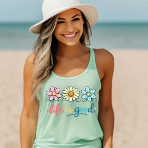 May include: A light green tank top with a floral design and the text "life is good". The flowers are pink, yellow, and blue. The tank top is a scoop neck style.